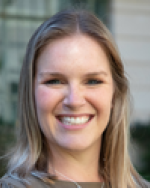 A photo of Jordan from the shoulders up while she is standing outside of a building and wearing a grey shirt.