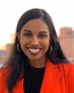 Photo of Meera Sam standing out in a bright red blazer, smiling
