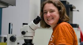 Abigail Jones sits in a lab beside a microscope.