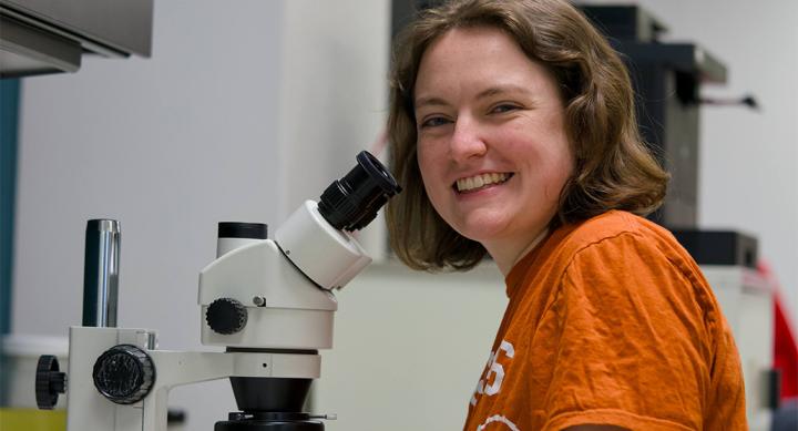 Abigail Jones sits in a lab beside a microscope.